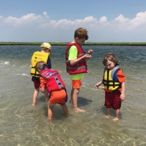 4 boys exploring the shallow water beach on the bay at summer camp by boat